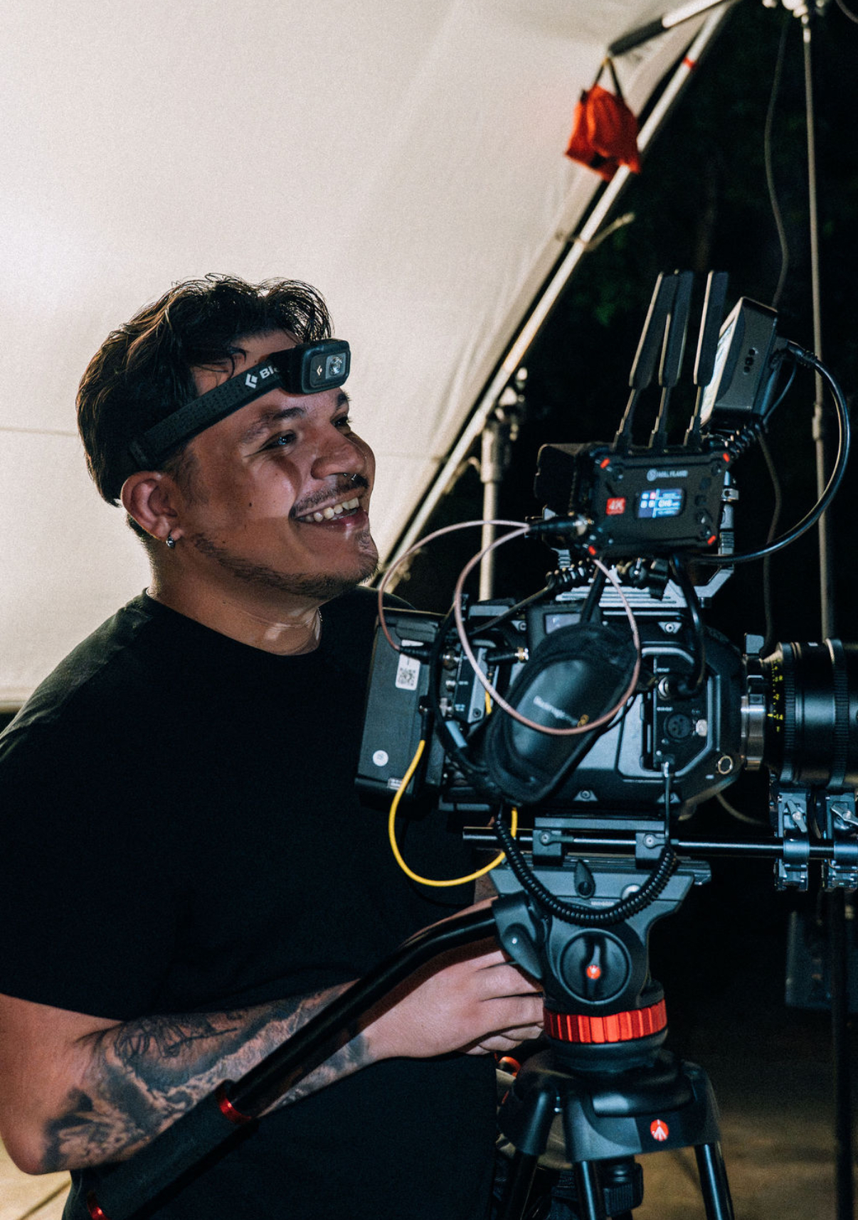 Jeremy smiling beside a cinema camera on a tripod, with lighting equipment in the background.